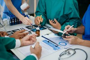 Medical team having a meeting with doctors in white lab coats and surgical scrubs seated at a table discussing a patients working online using computers in the medical industry photo