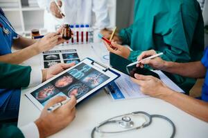 Medical team having a meeting with doctors in white lab coats and surgical scrubs seated at a table discussing a patients working online using computers in the medical industry photo
