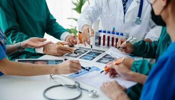 Medical team having a meeting with doctors in white lab coats and surgical scrubs seated at a table discussing a patients working online using computers in the medical industry photo