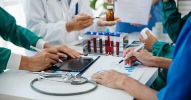 Medical team having a meeting with doctors in white lab coats and surgical scrubs seated at a table discussing a patients working online using computers in the medical industry photo