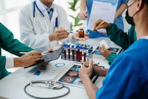 Medical team having a meeting with doctors in white lab coats and surgical scrubs seated at a table discussing a patients working online using computers in the medical industry photo