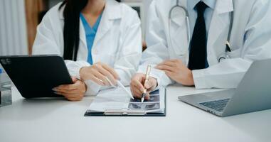 Medical team having a meeting with doctors in white lab coats and surgical scrubs seated at a table discussing a patients working online using computers in the medical industry photo