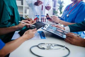 Medical team having a meeting with doctors in white lab coats and surgical scrubs seated at a table discussing a patients working online using computers in the medical industry photo