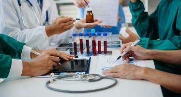 médico equipo teniendo un reunión con doctores en blanco laboratorio abrigos y quirúrgico matorrales sentado a un mesa que se discute un pacientes trabajando en línea utilizando ordenadores en el médico industria foto