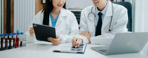 Medical team having a meeting with doctors in white lab coats and surgical scrubs seated at a table discussing a patients working online using computers in the medical industry photo