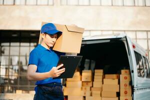 Smiling delivery man standing in front of his van with Holding Box and tablet delivery home and shipping photo