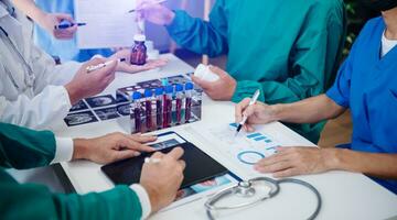 Medical team having a meeting with doctors in white lab coats and surgical scrubs seated at a table discussing a patients working online using computers in the medical industry photo