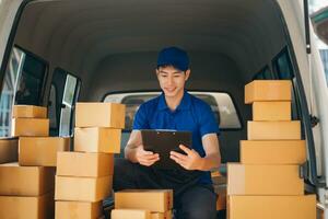 Smiling delivery man standing in front of his van with Holding Box and tablet delivery home and shipping photo