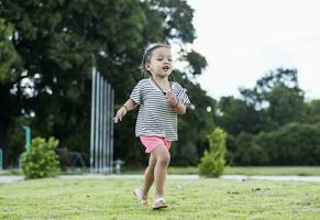 linda pequeño niña corriendo en el parque después colegio en el noche disfrutando jugando afuera. alegre asiático niños concepto foto