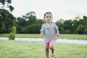 linda pequeño niña corriendo en el parque después colegio en el noche disfrutando jugando afuera. alegre asiático niños concepto foto