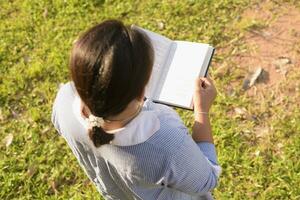 Girl reading a book in the front yard Female student portrait, education concept Happy cute kid smiling with learning. photo