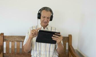 Mature Man outside sitting on a bench watching a show on his iPad Smart Tablet wearing headphones photo