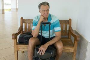 Mature Man sitting on a bench with his suitcase and backpack waiting for a ride photo