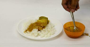 Female hand stirring Indian homemade mango curry rice with spoon on white plate. video