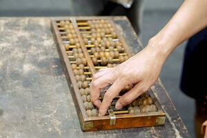 mano de persona jugando y demostración usado de antiguo chino ábaco en antiguo negro de madera mesa. foto