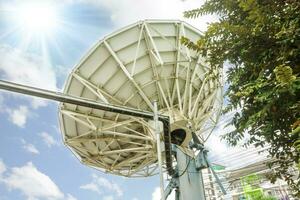 Back view of Grand Satellite dish at TV station under bright blue sky and sun flare background. photo