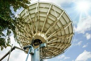 Back view of Grand Satellite dish at TV station under bright blue sky and sun flare background. photo