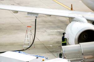 Closeup white airplane parked and refueling on ground in the airport with ground staff fixing. photo