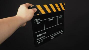 Hand is holding yellow and black color clapper board or movie slate on black background. photo