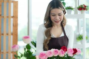 joven mujer florista oliendo un rojo Rosa en el flor tienda foto