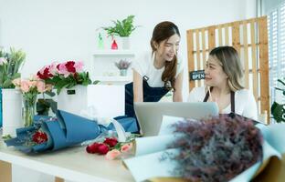 Two asian female florist working at flower shop with laptop. photo