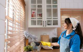 asiático joven mujer limpieza ventana en el cocina. tareas del hogar concepto foto