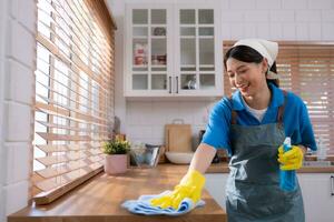 Cleaning service. Close-up of woman in apron and rubber gloves cleaning wooden table with spray photo