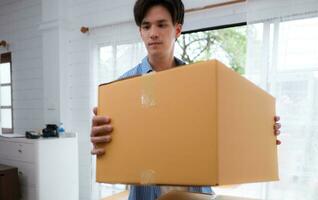 Young asian man holding cardboard box in his home. Concept move house photo