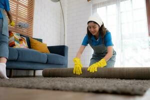 Young women cleaning maid in uniform and rubber gloves are cleaning the room, fold up carpet photo