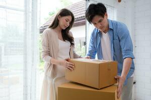 joven asiático Pareja Moviente en nuevo casa. asiático hombre y mujer participación cajas foto