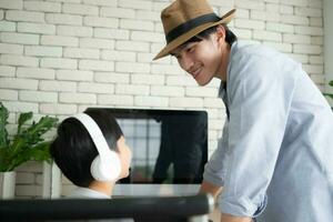 Son wearing headphones sits on computer desk chair with father, browsing for travel information for a weekend trip. photo