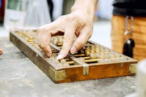 Closeup hand of person playing and demonstration used of ancient Chinese abacus on old black wooden table. photo