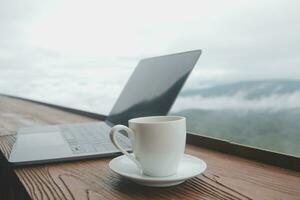 Young man freelancer traveler wearing hat anywhere working online using laptop and enjoying mountains view photo