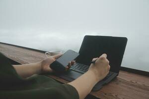 Young man freelancer traveler wearing hat anywhere working online using laptop and enjoying mountains view photo