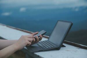 Young business woman working at the computer in cafe on the rock. Young girl downshifter working at a laptop at sunset or sunrise on the top of the mountain to the sea, working day. photo