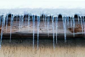 Icicles hang on a house roof. Snow melt from house roof warm winter day photo