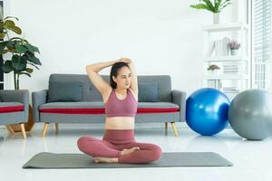 asiático joven sano mujer en material deportivo practicando yoga a hogar, deporte niña meditando en vivo habitación a hogar foto