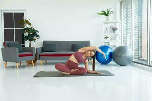 asiático joven sano mujer en material deportivo practicando yoga a hogar, deporte niña meditando en vivo habitación a hogar foto