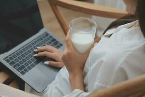Happy young female in casual clothes smiling and looking at camera while using laptop on bed in bedroom at home photo