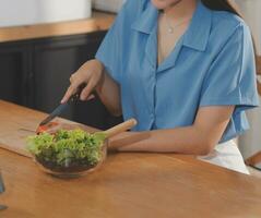 A young woman with a beautiful face in a blue shirt with long hair eating fruit sitting inside the kitchen at home with a laptop and notebook for relaxation, Concept Vacation. photo