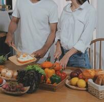 Handsome man sitting near his wife at kitchen. Family couple see social media, surf the web while sitting at kitchen table with generic laptop. Couple working with laptop at home photo