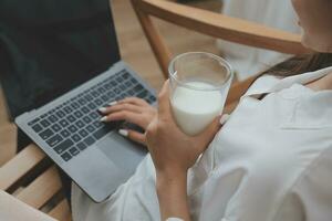 Happy young female in casual clothes smiling and looking at camera while using laptop on bed in bedroom at home photo