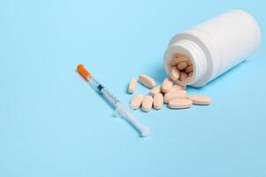 Studio shot of insulin syringe and pharmaceutical pills scattered from a white medicament container on blue background with copy space for medical ad for World Diabetes Awareness Day 14 November. photo