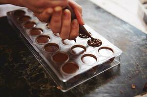 Pastry chef filling empty chocolate molds with filling for further preparation luxury homemade chocolate products photo
