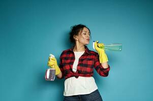 Attractive playful woman, a housewife, holds a cleaning spray in her hands like a gun and blows off gunpowder as if after a shot photo