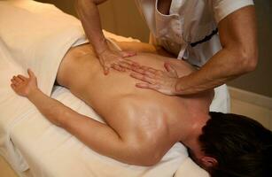 ayurvédico tratamiento, profesional terapéutico cuerpo masaje a el bienestar spa clínica. un joven hombre relaja mientras acostado en un masaje mesa durante un terapéutico espalda masaje a un lujo spa. foto
