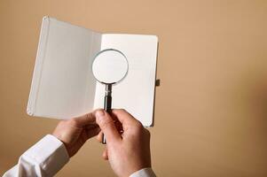 A view of an image of white blank sheet with a magnifier or magnifying glass in female hands. Beige background , copy space photo