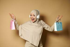 Happy Muslim woman raising arms with color bags in her hands, smiles looking at camera. photo