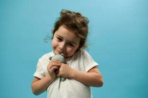 Beautiful little girl hugs her toy and looking down with sadness. Blue background photo