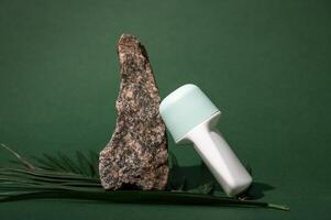 Still life with white mockup antiperspirant roller near a stone on a palm leaf, isolated on green studio background. photo